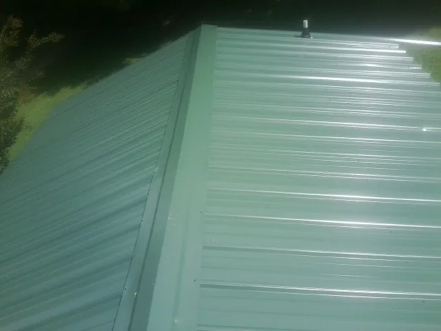 New green metal panels meeting at the ridge of a roof — Flat Roof Repair work by our crew in Harrisonville