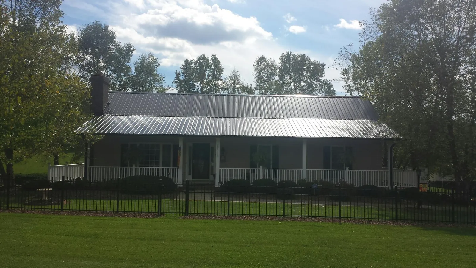 Gray metal roof on a brick ranch with a full width front porch — Gutter Guard Installation work by our crew in Harrisonville