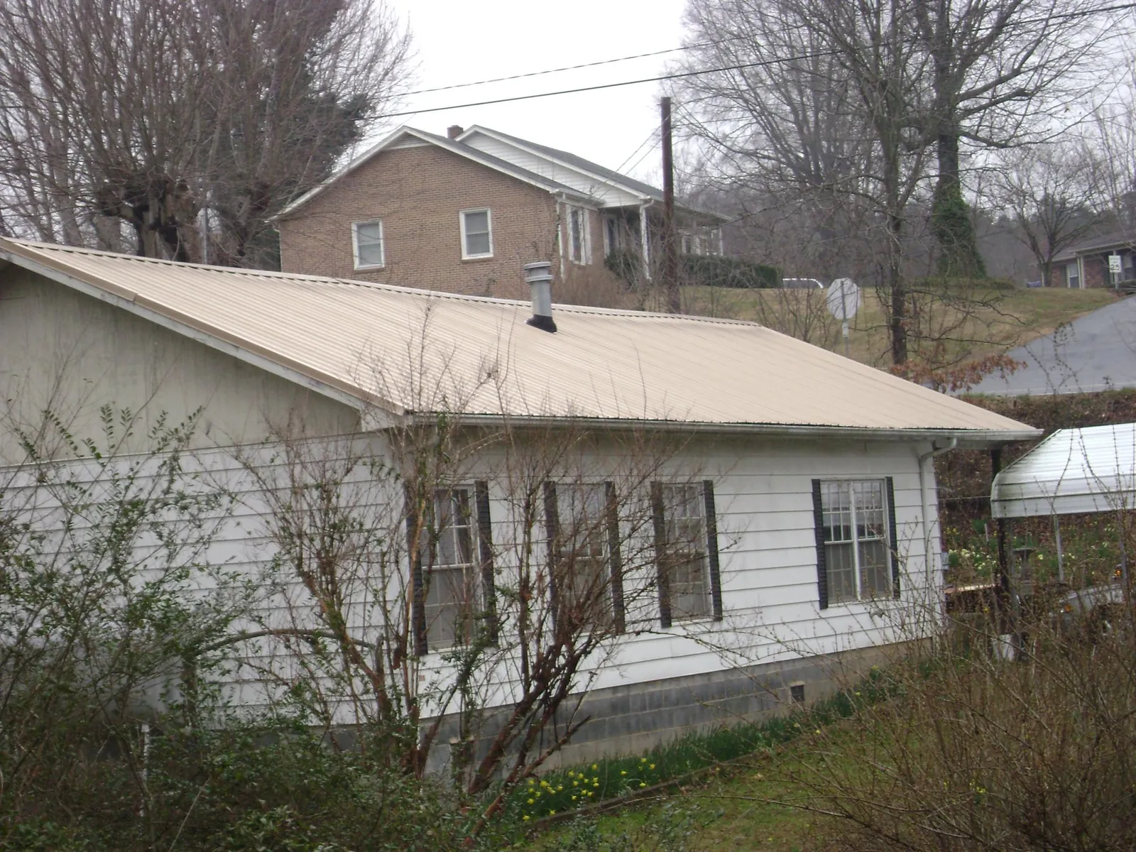 Tan metal roof on a white sided house set into a hillside — Commercial Roofing by Roofing Brothers in Harrisonville